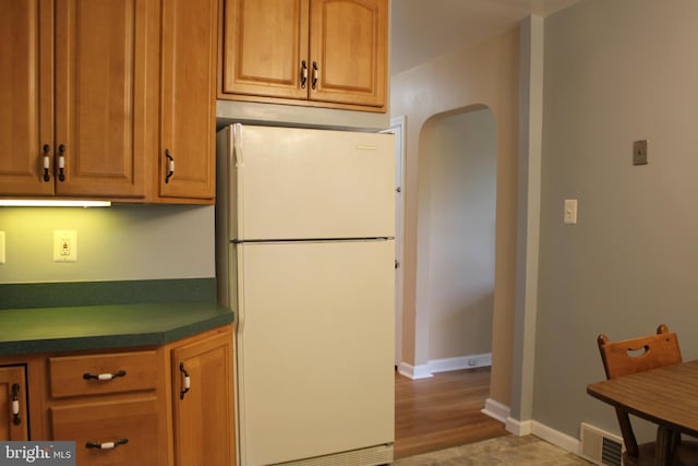 kitchen featuring freestanding refrigerator, dark countertops, baseboards, and brown cabinetry