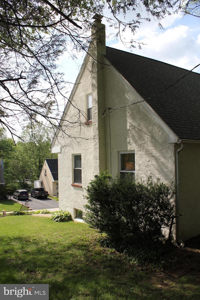 view of home's exterior featuring stucco siding, roof with shingles, a chimney, and a yard