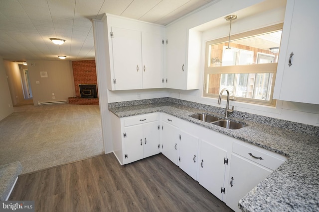 kitchen featuring dark wood-style flooring, baseboard heating, a fireplace, white cabinetry, and a sink