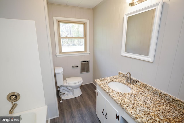 bathroom with vanity, toilet, heating unit, a bath, and wood finished floors