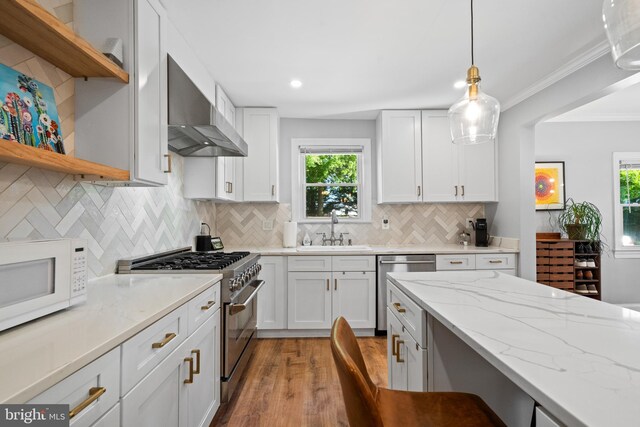 kitchen with wall chimney range hood, open shelves, a sink, stainless steel appliances, and light wood-style flooring