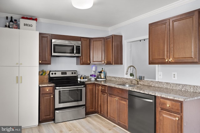 kitchen with light wood-type flooring, light stone countertops, appliances with stainless steel finishes, and a sink