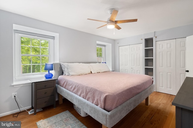 bedroom featuring two closets, baseboards, a ceiling fan, and wood finished floors