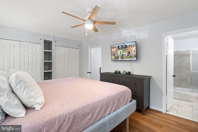bedroom featuring multiple closets, wood finished floors, ensuite bath, baseboards, and ceiling fan