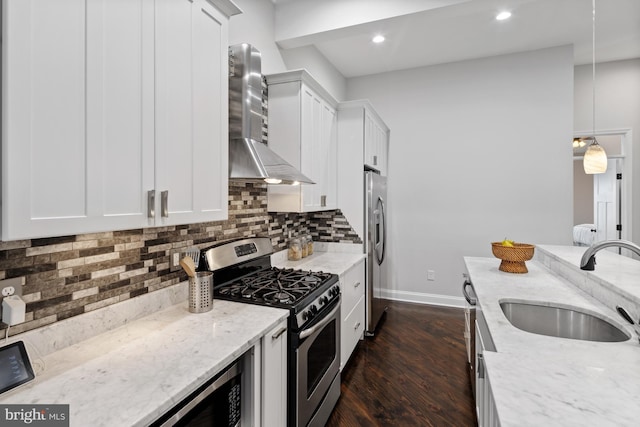 kitchen with stainless steel appliances, wall chimney range hood, dark wood-style flooring, a sink, and baseboards