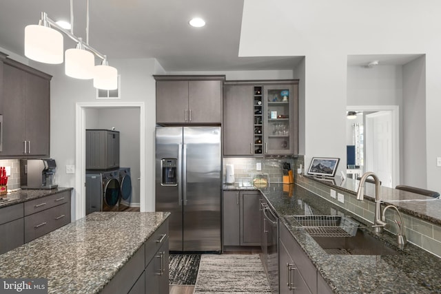 26325 Tributary Blvd, Millsboro, DE 19966 - kitchen featuring appliances with stainless steel finishes, washer and clothes dryer, a sink, backsplash, and dark stone countertops
