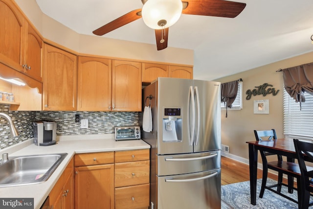 kitchen featuring a ceiling fan, wood finished floors, a sink, stainless steel fridge, and light countertops