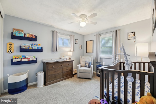carpeted bedroom with baseboards, a ceiling fan, a crib, and a textured ceiling
