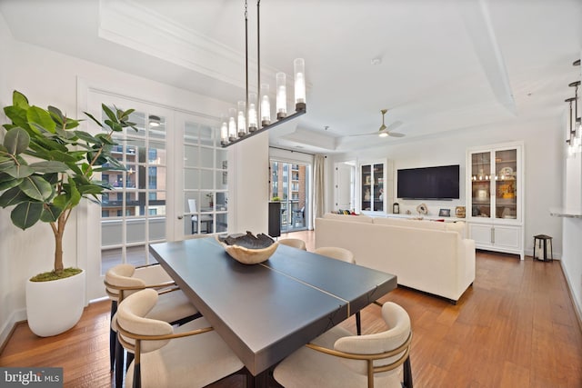dining area with a ceiling fan, a raised ceiling, and wood finished floors