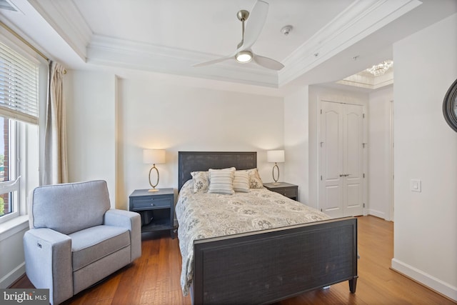 bedroom with crown molding, multiple windows, a tray ceiling, and wood finished floors