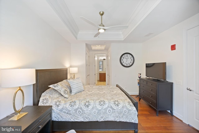 bedroom featuring ceiling fan, baseboards, wood finished floors, a tray ceiling, and ornamental molding