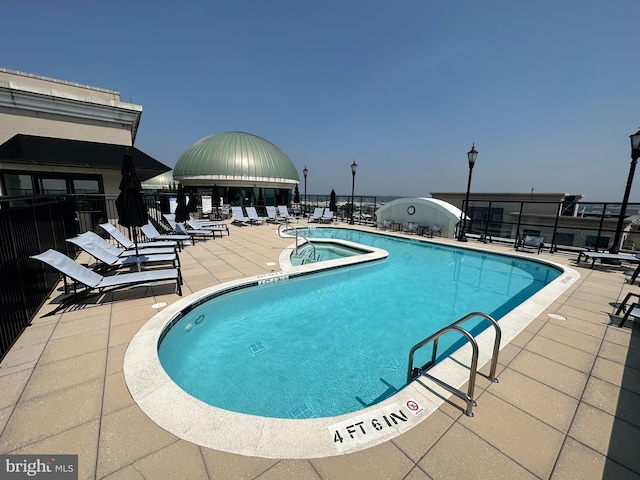 community pool with fence, a patio, and a hot tub