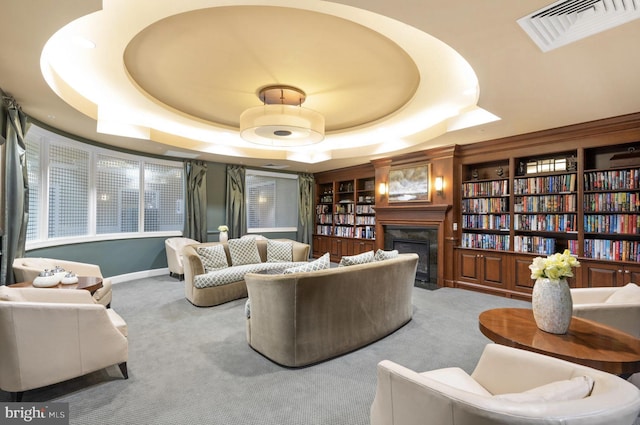 living area featuring visible vents, built in features, a fireplace, a tray ceiling, and carpet flooring