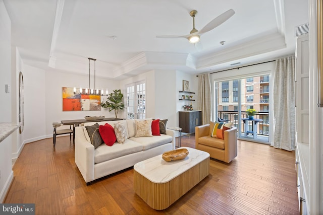 living area featuring light wood-style flooring, a raised ceiling, ceiling fan with notable chandelier, and ornamental molding
