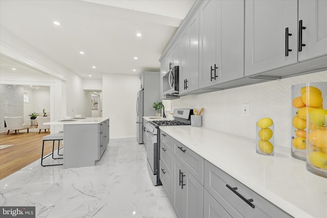 kitchen with a center island, appliances with stainless steel finishes, a kitchen breakfast bar, gray cabinetry, and backsplash