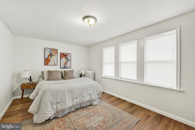 bedroom featuring radiator heating unit, baseboards, and wood finished floors