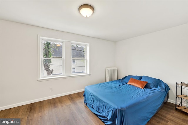 bedroom featuring baseboards, radiator, and wood finished floors