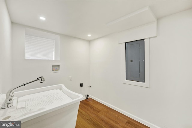 clothes washing area with electric panel, washer hookup, laundry area, a sink, and wood finished floors