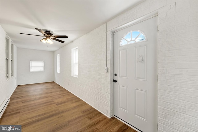 entryway with a wealth of natural light, brick wall, wood finished floors, and ceiling fan