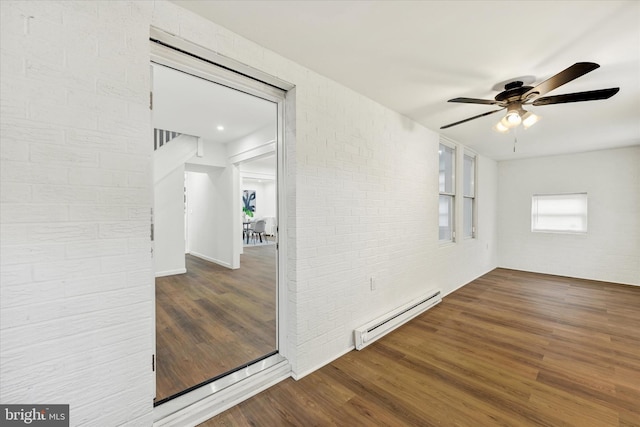 spare room featuring a baseboard radiator, wood finished floors, ceiling fan, and brick wall