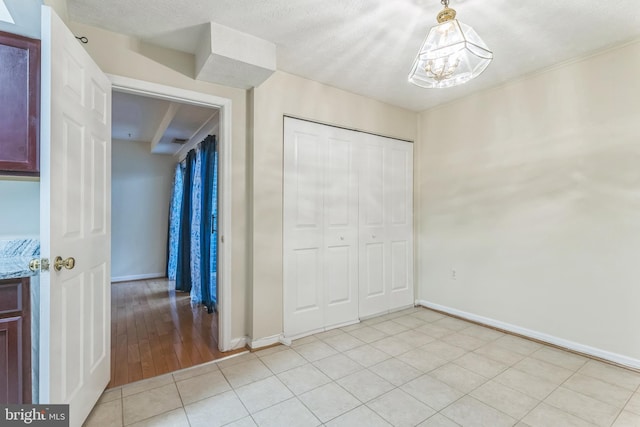 unfurnished bedroom featuring a chandelier, light tile patterned floors, baseboards, and a closet