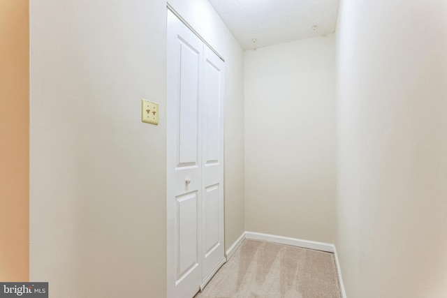 corridor with light carpet, baseboards, and a textured ceiling