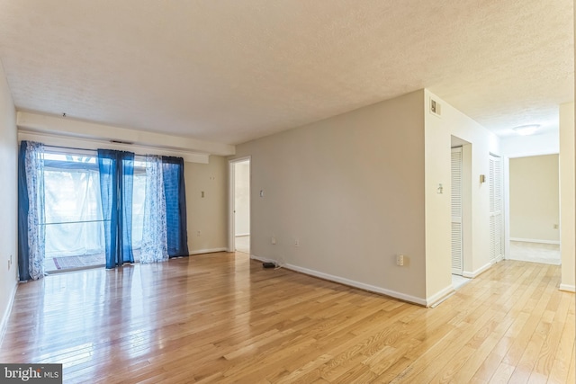 empty room featuring light wood finished floors, visible vents, and baseboards