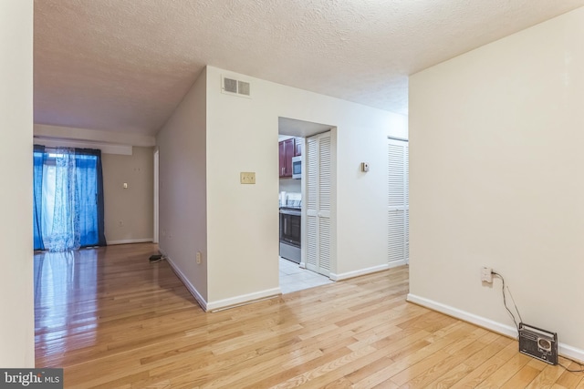 empty room featuring light wood-style floors, baseboards, visible vents, and a textured ceiling