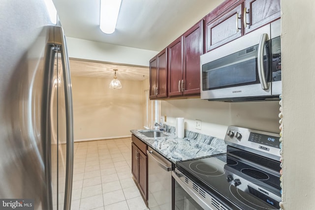 kitchen featuring dark brown cabinets, appliances with stainless steel finishes, light tile patterned flooring, a sink, and light stone counters
