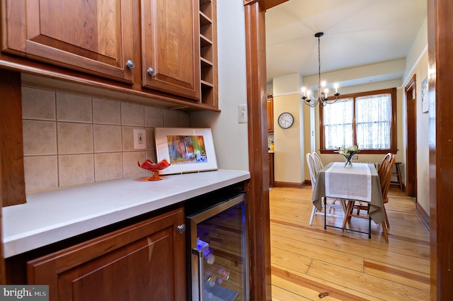 kitchen with beverage cooler, decorative backsplash, light countertops, light wood-style floors, and a chandelier