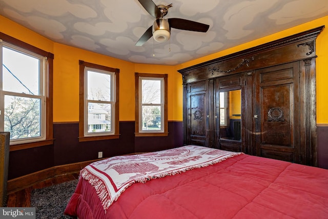 bedroom with a wainscoted wall, multiple windows, wood finished floors, and ceiling fan