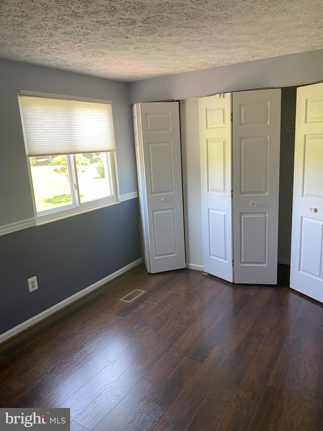 unfurnished bedroom featuring a textured ceiling, dark wood finished floors, baseboards, and a closet