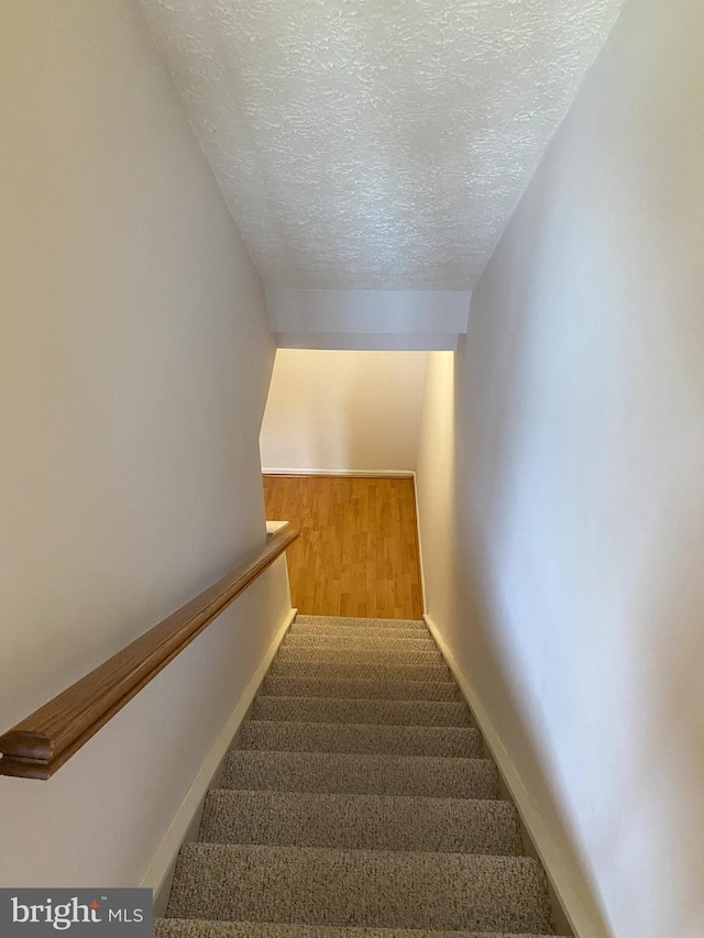 staircase featuring a textured ceiling, carpet floors, and baseboards