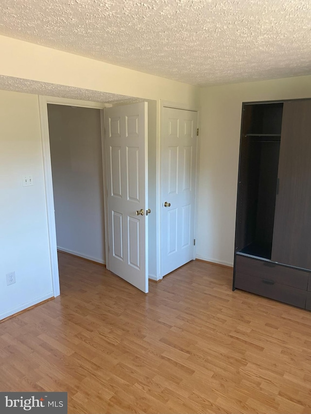 unfurnished bedroom featuring light wood-type flooring, baseboards, and a textured ceiling