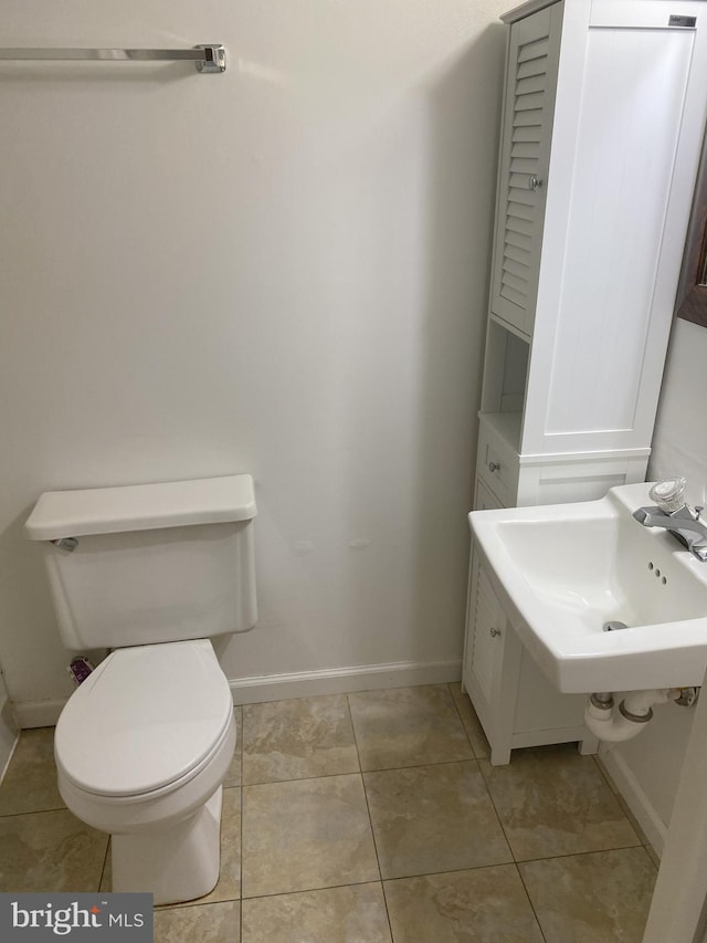 bathroom featuring baseboards, toilet, a sink, and tile patterned flooring