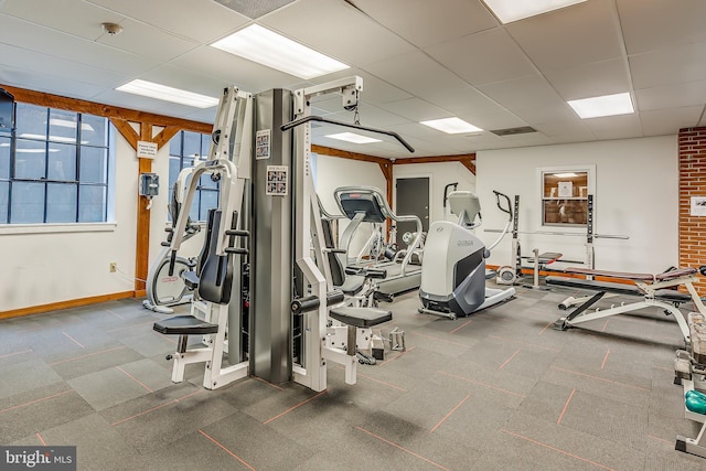 exercise room featuring a paneled ceiling and baseboards
