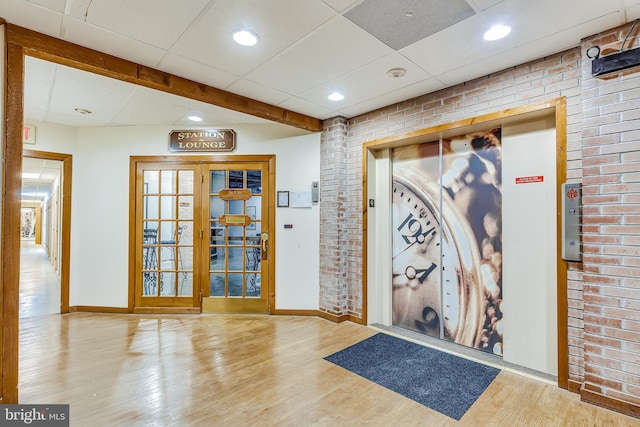 interior space featuring elevator, baseboards, brick wall, a paneled ceiling, and wood finished floors