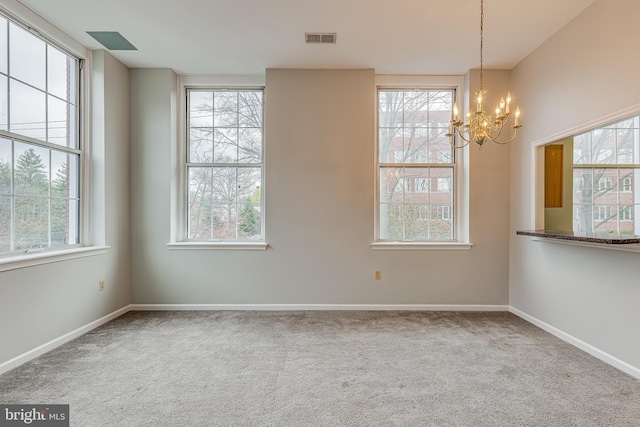 carpeted spare room featuring visible vents, a wealth of natural light, a notable chandelier, and baseboards