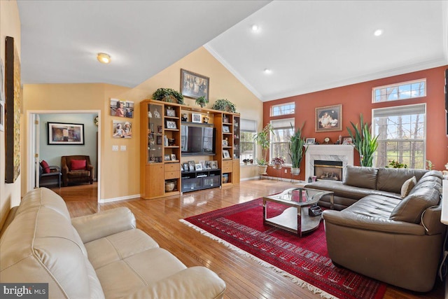 living area with high vaulted ceiling, a wealth of natural light, ornamental molding, and light wood-type flooring