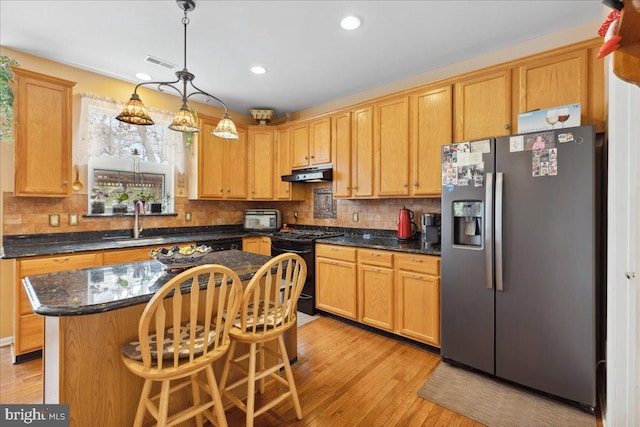 kitchen featuring black range with gas stovetop, a sink, stainless steel refrigerator with ice dispenser, under cabinet range hood, and visible vents