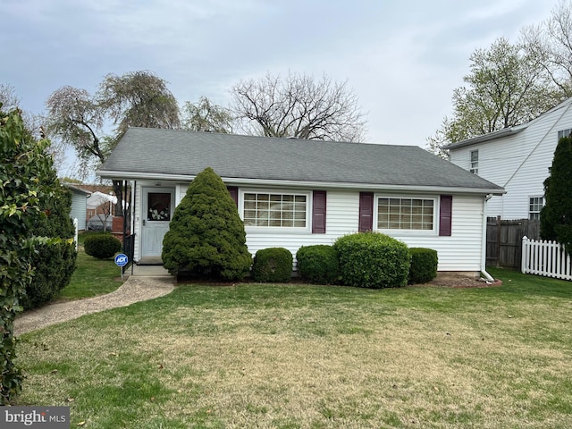 view of front facade featuring roof with shingles, fence, and a front lawn
