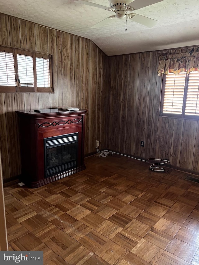 unfurnished living room with a fireplace, a textured ceiling, wood walls, visible vents, and ceiling fan