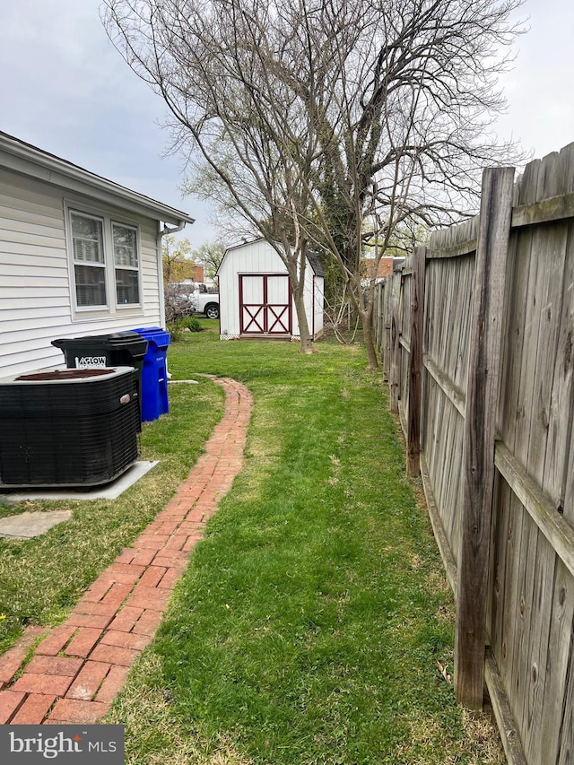 view of yard featuring a shed, central AC unit, a fenced backyard, and an outbuilding