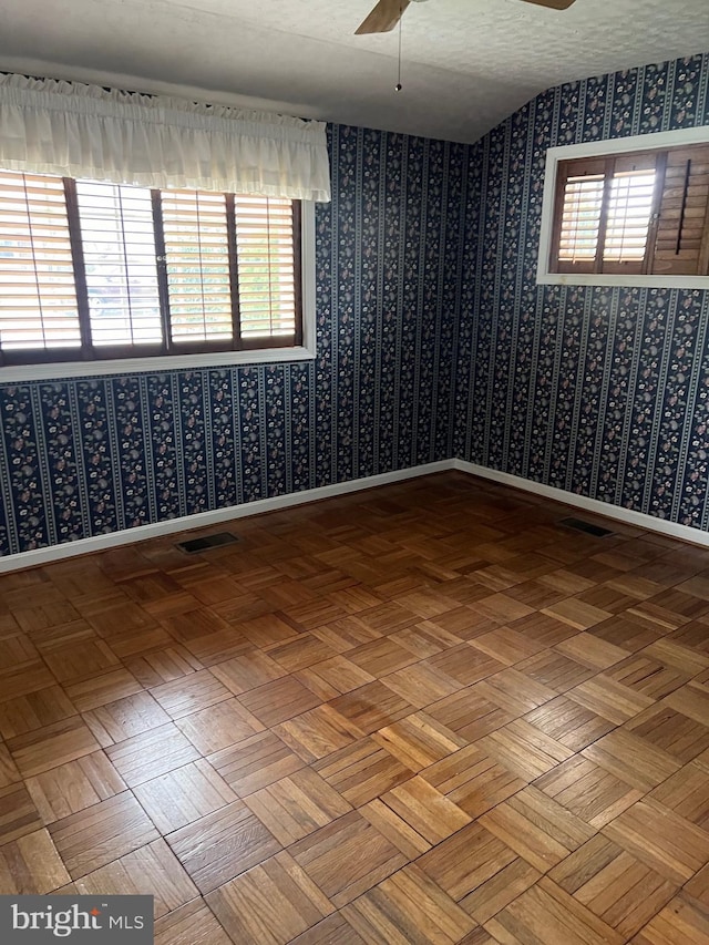 empty room featuring visible vents, a ceiling fan, and wallpapered walls