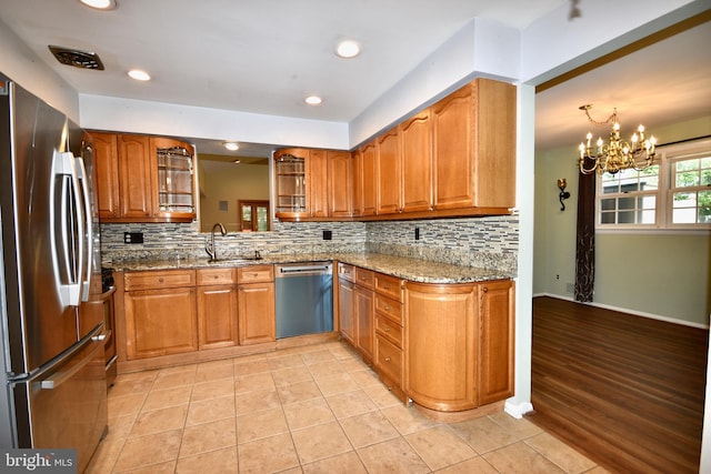 kitchen featuring light stone countertops, brown cabinets, a sink, backsplash, and stainless steel appliances