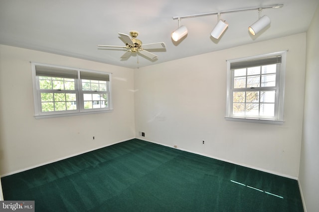 empty room featuring dark carpet, baseboards, ceiling fan, and a healthy amount of sunlight
