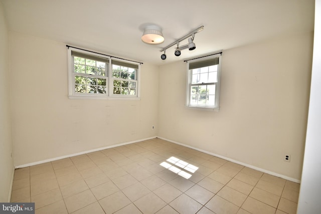spare room featuring a healthy amount of sunlight, light tile patterned floors, baseboards, and rail lighting