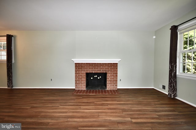 unfurnished living room with a brick fireplace, baseboards, visible vents, and wood finished floors