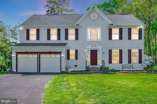 colonial-style house with an attached garage, driveway, a shingled roof, and a front lawn