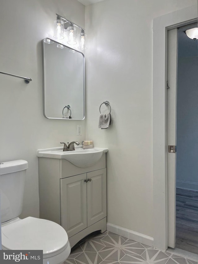 half bathroom with baseboards, toilet, and vanity